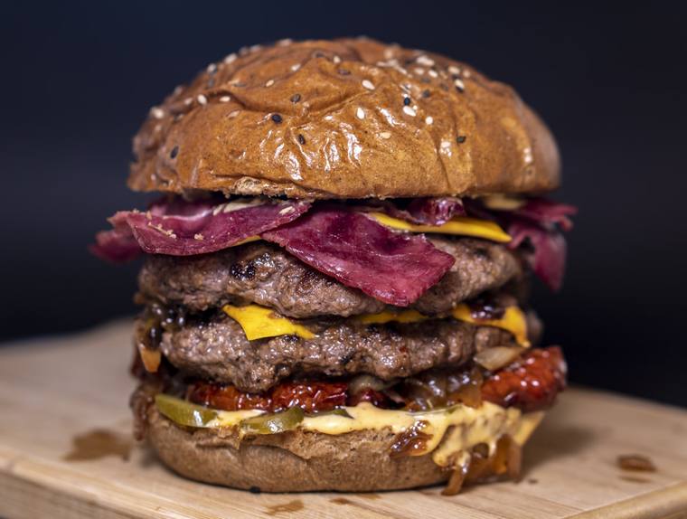 Dubbele burger met kaas, gegrild vlees en saus op een houten plank