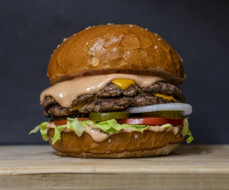 Dubbele hamburger met kaas, saus, augurk en tomaat op een houten plank